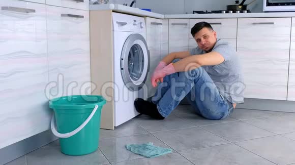 穿着橡胶手套的疲惫的人坐在厨房地板上打扫卫生休息一下视频的预览图