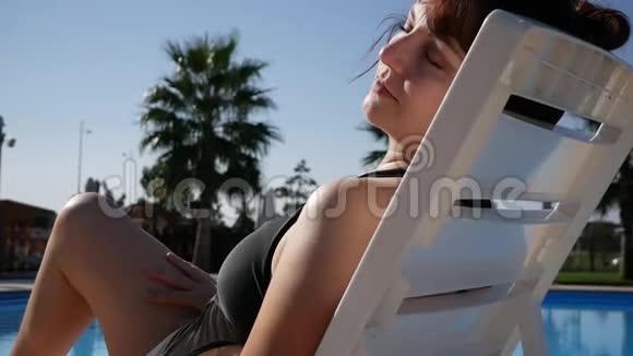 在海滩度假酒店享受夏日触摸光滑的脱毛腿在泳池边晒日光浴的女士视频的预览图