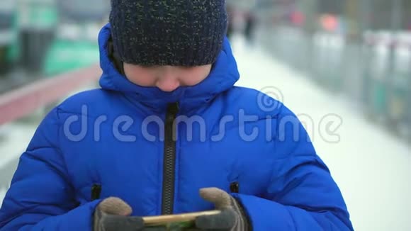 穿着蓝色羽绒服的少年在街上看智能手机他去看镜头视频的预览图