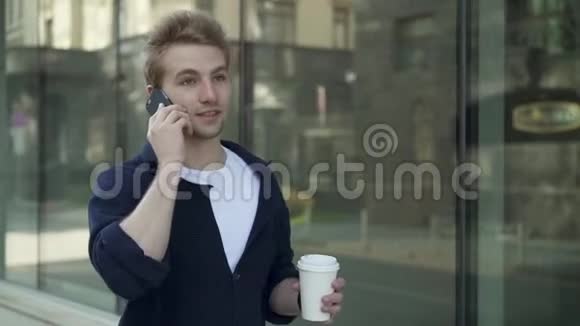 带着咖啡的年轻人走在大楼里打电话视频的预览图
