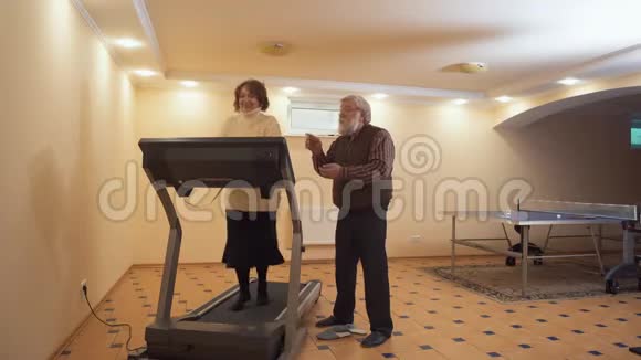 一位老年妇女试图在跑步机上跑步她的灰头发的丈夫站在旁边用爱和支持看着她视频的预览图