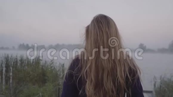 一个年轻的女人走向湖边她的长发随风飘扬视频的预览图