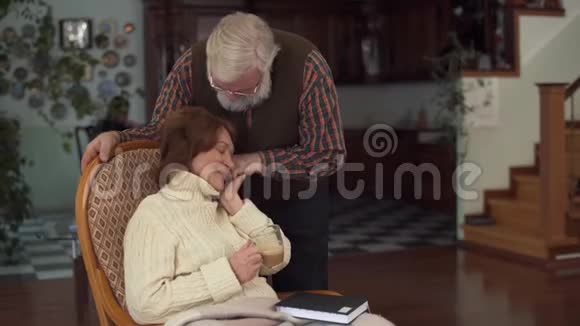 成熟的女人坐在现代化的大房子里的摇椅里她丈夫站在附近温柔地握住她的手高级视频的预览图