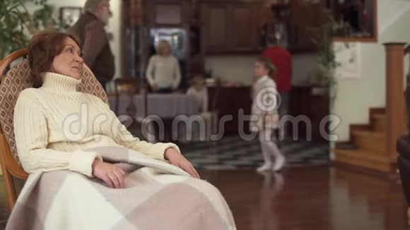 成熟的女人坐在现代化的大房子里的摇椅里她丈夫和两个孙子都在后台奶奶视频的预览图