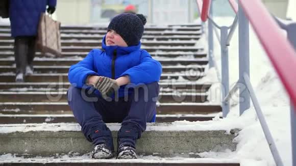 穿着蓝色羽绒服的少年在城里迷路了他坐在冰冷的楼梯上环顾四周视频的预览图