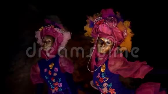 两个穿着鲜艳服装戴着鲜花和金色面具的年轻女孩跳舞挥舞着双手他们晚上跳舞视频的预览图