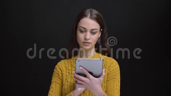 身着黄色毛衣的长发黑发女孩的肖像微笑着将绿色的平板电脑屏幕放在黑色相机上视频的预览图