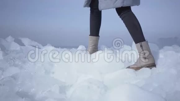 穿着温暖夹克和靴子的无法辨认的女人的腿爬上冰川走在边缘奇妙的大自然视频的预览图