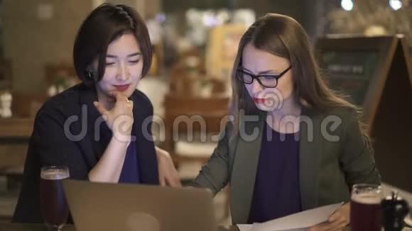 两个漂亮的同事一起用笔记本电脑在咖啡馆工作视频的预览图