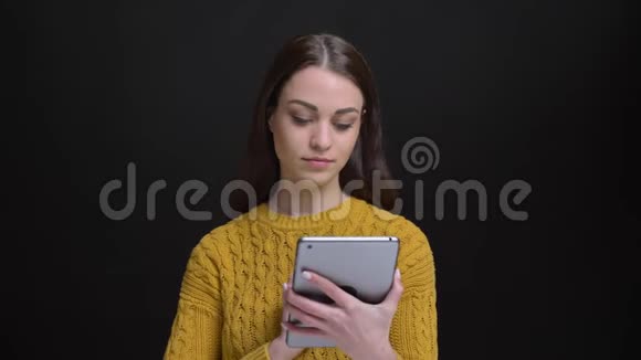 身着黄色毛衣的长发黑发女孩的肖像欢快地将绿色的平板电脑屏幕显示在黑色相机中视频的预览图