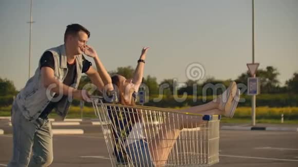 快乐的人日落时分一对夫妇一男一女骑在超市的手推车上慢行视频的预览图