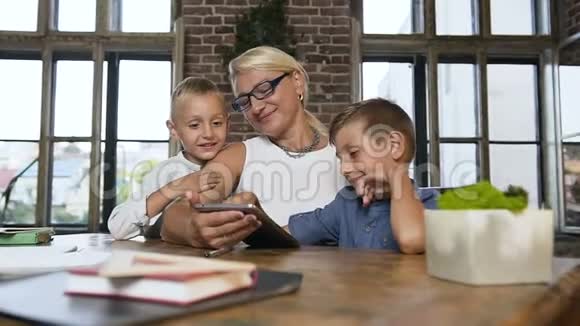 戴眼镜的白人商业中年妇女和她的孙子们坐在舒适的办公室里的桌子旁视频的预览图