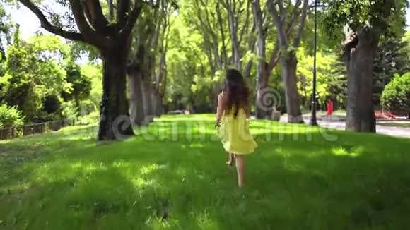 快乐的小女孩穿着黄色连衣裙光着脚在公园的绿草上奔跑视频的预览图