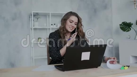 年轻讨人喜欢的女商人带着笔记本电脑在办公室打电话在报纸上写笔记重点视频的预览图