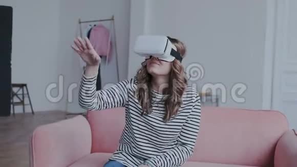 漂亮的年轻女性戴着虚拟现实眼镜玩游戏女士使用3D虚拟现实耳机她坐在沙发上视频的预览图