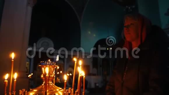 年轻的基督教妇女在教堂前祈祷的图标与烛光背景慢动作视频的预览图
