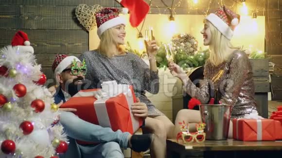 有胡子的男人坐在椅子上手里拿着一份很棒的礼物两个戴着帽子的白人女孩在新年上喝香槟视频的预览图