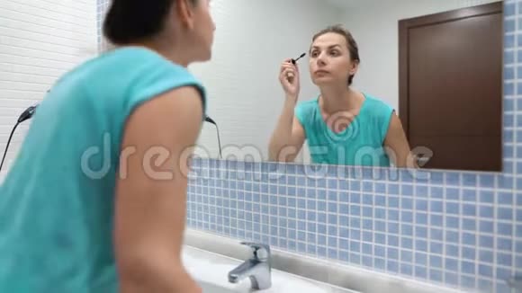在浴室镜子前用黑色睫毛膏化妆的漂亮女人视频的预览图