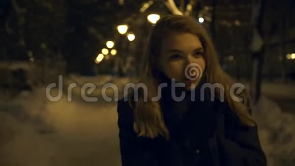 寂寞的年轻女子在白雪皑皑的冬城公园里散步夜晚在灯光下的黄光下视频的预览图