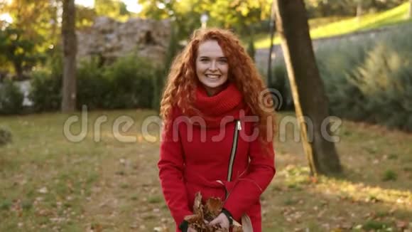 一个快乐的红头女人在秋天的一天里到处扔树叶抬头看秋天的树叶飘落视频的预览图