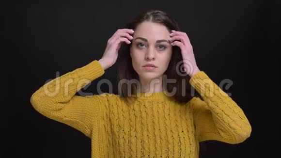 一幅长头发的黑发女孩的肖像穿着黄色毛衣梳着头发时尚地摆在黑色相机上视频的预览图
