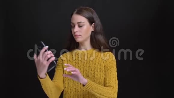 身着黄色毛衣的长发黑发女孩用黑色智能手机快乐地制作自拍照片的肖像视频的预览图