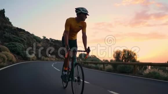 一个年轻的运动员骑着自行车骑在山蛇形上穿着黄色的t恤和运动衫看着相机视频的预览图