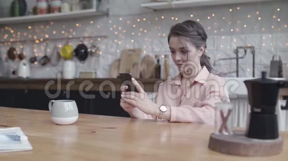 一个年轻的女人带着手机和一杯咖啡在厨房沟通的概念库存录像青年视频的预览图