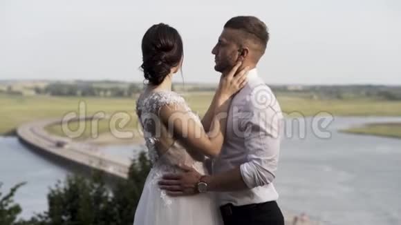 时尚的新娘和新郎在河流和绿色草地的背景上摆姿势爱和家庭的概念行动感性视频的预览图