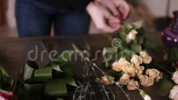 专业的花艺师花艺师从多余的叶子中清洗花朵花店车间的淡黄色玫瑰视频的预览图