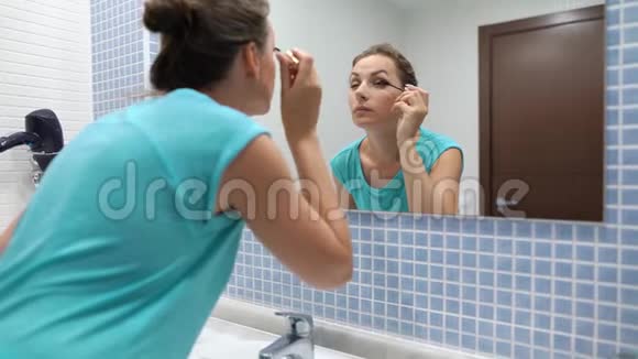 在浴室镜子前用黑色睫毛膏化妆的漂亮女人视频的预览图