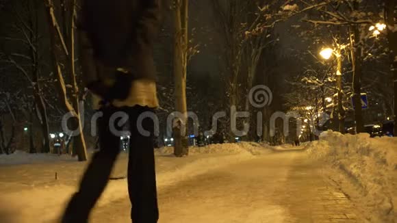 寂寞的年轻女子在白雪皑皑的冬城公园里散步夜晚在灯光下的黄光下视频的预览图