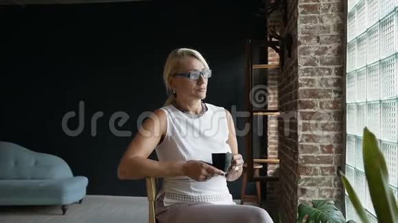 可爱的老妇人正坐在窗边喝着咖啡神情愉快地看着外面成熟的商业女性视频的预览图