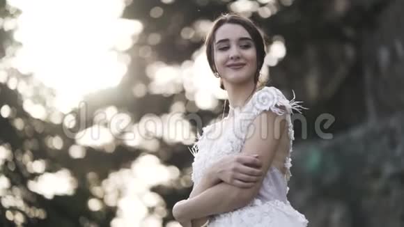 美丽的新娘穿着婚纱在模糊的背景下明亮的天空和绿色的树叶婚姻的概念行动A视频的预览图