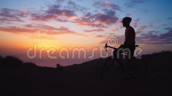 年轻的运动员坐在山顶上的自行车上戴着黄色的t恤头盔和运动器材看着视频的预览图