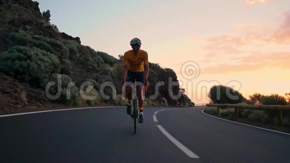 一个年轻的运动员骑着自行车骑在山蛇上戴着黄色的t恤头盔和运动装备看着视频的预览图