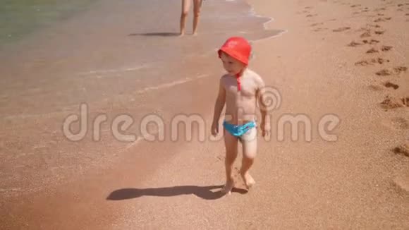 4k慢动作视频欢笑欢快的幼儿男孩在沙滩上漫步大海视频的预览图