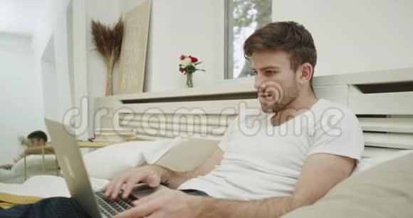 好人有一个工作时间在他的床上穿着睡衣和使用他的笔记本敲击键盘视频的预览图