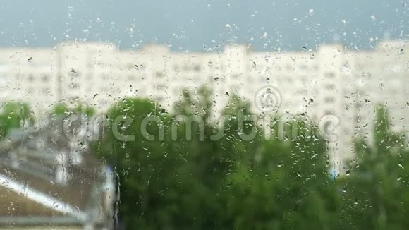 窗户玻璃上的水滴城市里的夏雨模糊的房屋轮廓和绿树4K视频视频的预览图