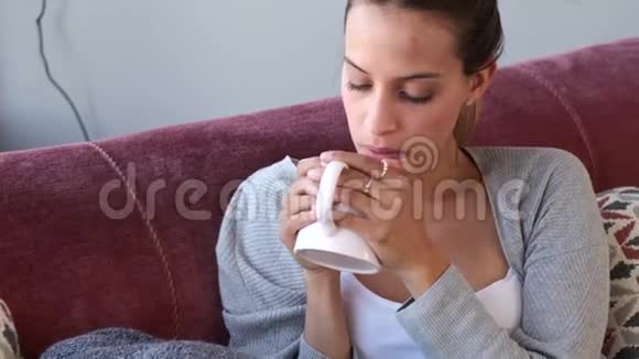 严肃的年轻女子透过窗户一边在家里的沙发上喝咖啡视频的预览图
