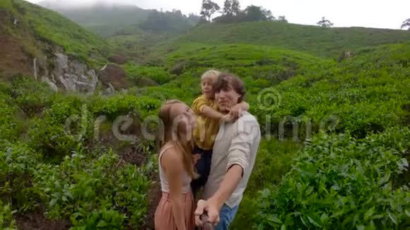慢镜头年轻夫妇和他们的儿子站在山上的一个大茶园里自拍视频的预览图