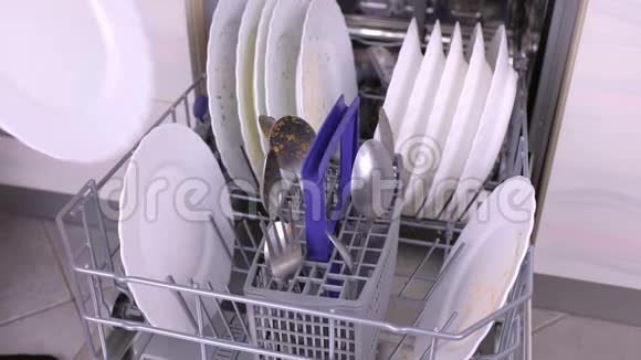 男人手在洗碗机里放一个白色的脏盘子和勺子然后在厨房里运行视频的预览图