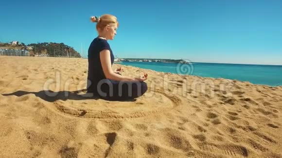 年轻女子在海边坐着莲花姿势运动女孩练习瑜伽视频的预览图