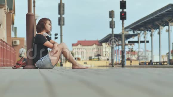 悲伤的女孩坐在火车站的瓷砖上戴着耳机视频的预览图