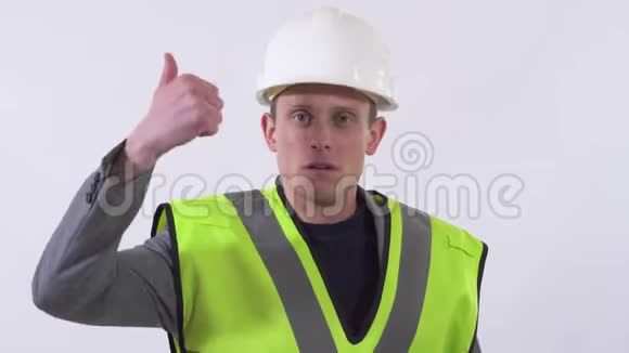 一个穿着建筑工服头上戴着白色头盔的自信男人的肖像他的拇指被孤立在白色上视频的预览图