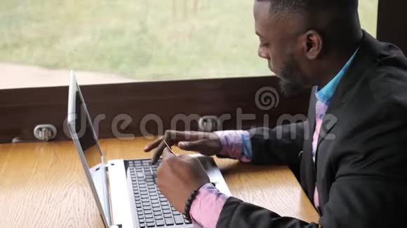 黑人在笔记本电脑上做支付银行卡在线购买在咖啡馆购物视频的预览图