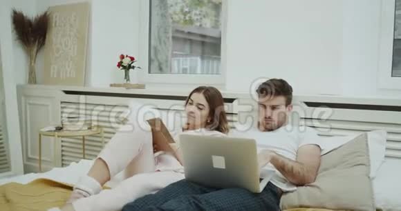 一对夫妇在床上的早晨例行公事女士读一本书男人在他的笔记本上检查一些东西视频的预览图