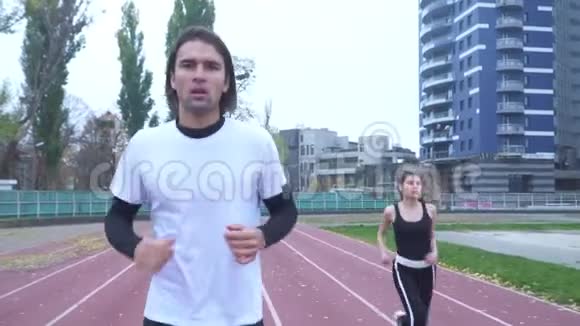 一个穿着紧身运动衫和裤子的黑发女孩超过了跑步的人一个穿着一件运动衫的年轻人视频的预览图