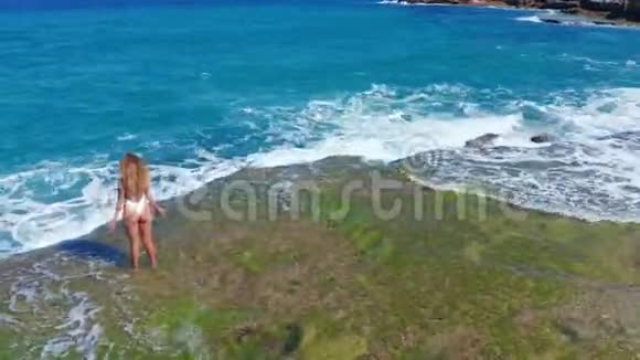 空中观景性感女孩站在洛基海滩的悬崖上一个女人看向远处视频的预览图