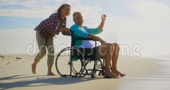 积极的高加索夫妇在海滩上用手机自拍的侧面视图4k视频的预览图